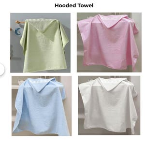 Op de afbeelding: Vier badhanddoeken met capuchon in verschillende kleuren: groen, roze, lichtblauw en wit. De groene handdoek heeft een wit kroonontwerp. De handdoeken hangen aan een rek.