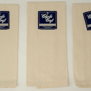 May include: Three cream-colored Charles Craft kitchen towels. Each towel has a textured weave and a dark blue tag with white text. The tags read "Charles Craft" and "100% Cotton".