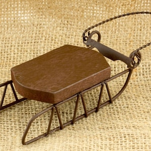 May include: A small, rustic-looking metal sled with a wooden seat. The sled is brown and has a wire frame.