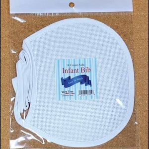 May include: White 14 count Aida fabric for cross stitch, shaped like a bib for a baby. The package has a label that says "Infant Bib" and "Easy To Stitch".