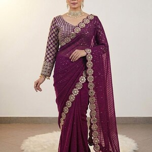 May include: A formal purple saree with intricate gold embroidery and embellishments. The saree features a matching long-sleeved blouse with detailed patterns. The design includes a decorative border and a sheer, flowing fabric.