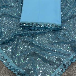 Puede incluir: Una tela de color turquesa con un dise&ntilde;o de lentejuelas y una tela azul claro. La tela turquesa tiene un borde festoneado. La tela azul claro tiene un ribete decorativo. Es probable que las telas formen parte de una prenda.
