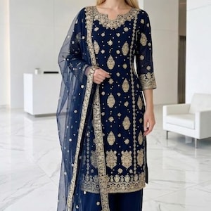 Puede incluir: Conjunto de salwar kameez azul marino bordado en oro. El atuendo incluye una túnica, pantalones y una dupatta transparente, todos adornados con intrincados diseños dorados. Las mangas tres cuartos y los pantalones a juego crean un look coordinado.