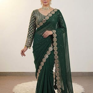 May include: Emerald green saree with intricate gold embroidery along the borders and sleeves. The saree features a sheer, flowing fabric with a detailed pattern. The long sleeves and neckline are adorned with gold embellishments, creating an elegant look.