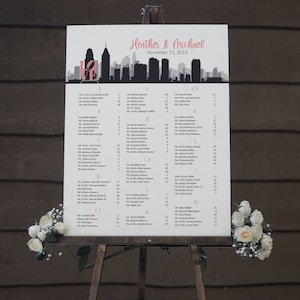 May include: A white wedding seating chart with a black and gray cityscape silhouette at the top. The chart lists the names of wedding guests and their table assignments. The text at the top reads "Heather & Michael, November 12, 2012".