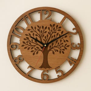 May include: A circular wooden wall clock with a tree of life motif. The clock has a light brown wood finish, cut-out numerals, and a tree silhouette at the centre. The clock hands are black, and the second hand is red.