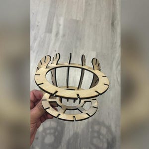 Puede incluir: Un objeto decorativo de madera cortado con l&aacute;ser con un dise&ntilde;o circular. El objeto presenta m&uacute;ltiples capas y soportes verticales, creando una estructura abierta en forma de jaula. El color natural de la madera es visible.