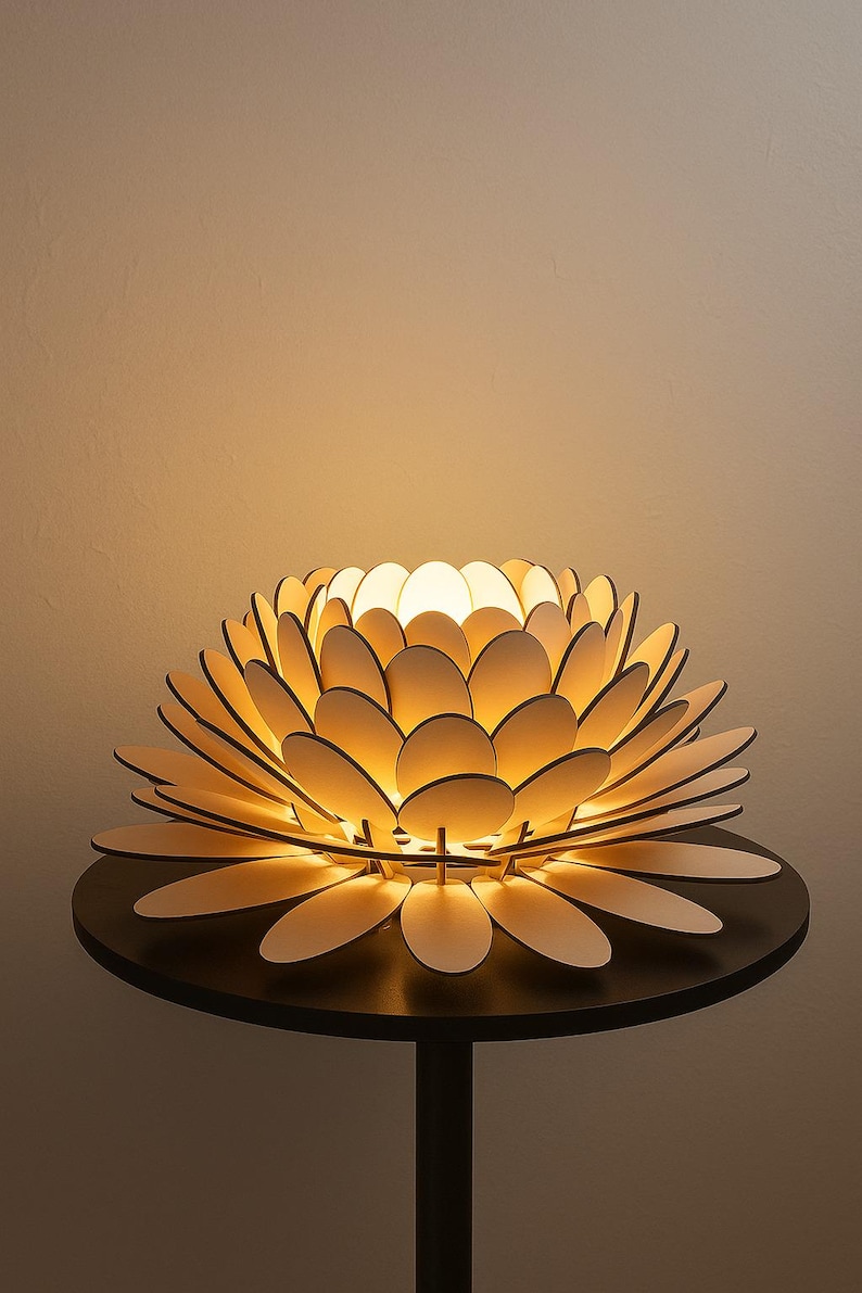 Puede incluir: Una l&aacute;mpara de madera con forma de flor con p&eacute;talos superpuestos, iluminada desde el interior. La l&aacute;mpara est&aacute; sobre una peque&ntilde;a mesa redonda negra. Los p&eacute;talos son de color claro y la luz crea un brillo c&aacute;lido.