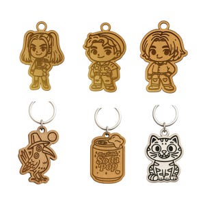 May include: A collection of six wooden keychains. The keychains feature various designs, including cartoon figures, a bird, a soda can with the text "My Little Soda Pop", and a cat. Each keychain has a silver metal ring.