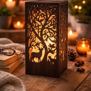 May include: A dark brown, rectangular wooden lantern with a tree and deer silhouette design. The lantern has cut-out details that allow the warm light from within to shine through. The lantern is on a wooden surface.
