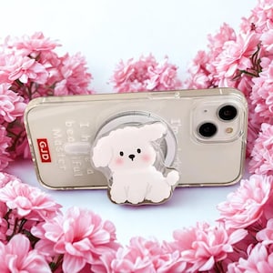 May include: A clear phone case with a white pop socket featuring a cartoon dog design. The phone case has the text "I'm a Beautiful Master" and the letters "GJD". The background is surrounded by pink flowers.