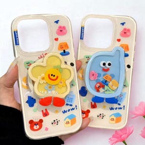 Pode incluir: Duas capas de telefone transparentes com desenhos de desenhos animados coloridos. Uma apresenta uma flor amarela com um rosto sorridente e pés vermelhos. A outra tem um personagem de telefone azul. Ambas as capas têm a palavra "Wow!" e outros gráficos pequenos.