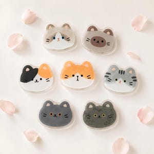 May include: Seven acrylic cat-shaped pins or charms featuring various feline coat patterns including calico, tabby, solid grey, and colour-point designs. Each piece displays a unique illustrated cat face with distinct eye colours and markings.
