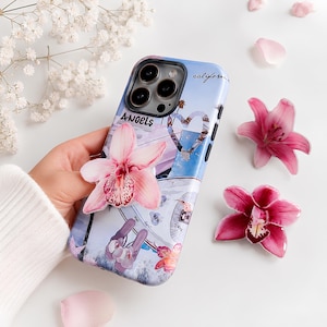Peut inclure: Une coque de téléphone avec un collage représentant une scène de plage, un cœur et les inscriptions "ANGELS" et "california". La coque est ornée d'une fleur d'orchidée rose en relief et entourée de pétales de lys roses épars.