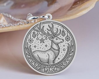 Op de afbeelding: Een zilveren hangerketting met een gedetailleerd gegraveerd ontwerp van een rendier met geweien, omringd door sterren, ornamenten en bellen. De ronde hanger is bevestigd aan een delicate ketting. De ketting is waarschijnlijk gemaakt van sterling zilver.