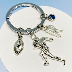 May include: Silver keyring with a football, a football player charm, a letter 'R' charm, and a blue rhinestone charm.