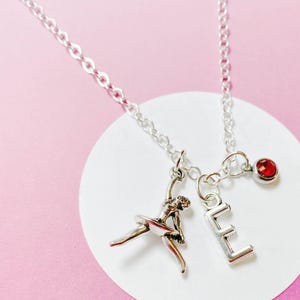 Puede incluir: Collar de plata con un dije de bailarina, un dije de la letra E y un dije de piedra roja.