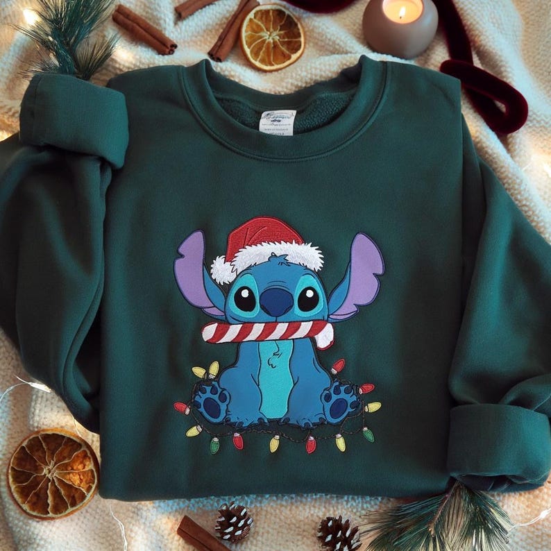 May include: A dark green sweatshirt featuring a cartoon character, Stitch, wearing a Santa hat and holding a candy cane. Stitch is surrounded by a string of colorful Christmas lights. The sweatshirt is a festive holiday item.
