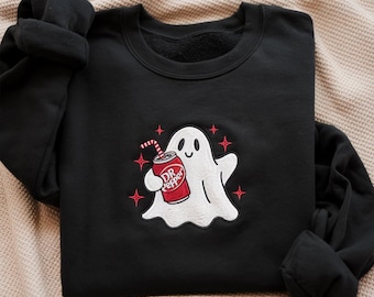 May include: Black sweatshirt with a white ghost holding a Dr. Pepper can. The ghost has a smiling face and is surrounded by four red starbursts. The Dr. Pepper can is red and white with a straw.