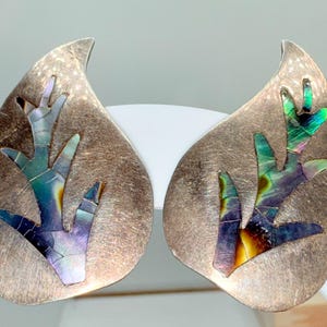 May include: Pair of silver-toned earrings with a leaf-like shape. Each earring features a mosaic design of iridescent abalone shell in shades of blue, green, and purple, resembling a stylized branch.