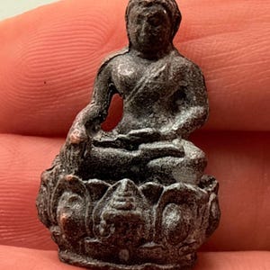 May include: A small, dark-colored Buddha statue seated in a meditative pose atop a lotus flower base. The statue has detailed facial features and is likely made of metal. The overall aesthetic suggests a focus on spirituality and Eastern religious themes.