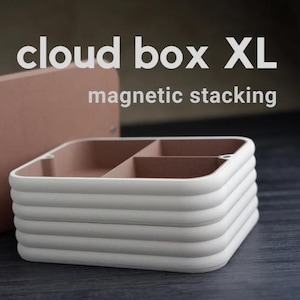 May include: A white, multi-tiered, rectangular box with a brown lid. The box has a magnetic closure and is labelled "cloud box XL magnetic stacking".