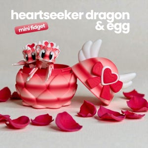 May include: A heartseeker dragon mini fidget toy and a matching egg container. The dragon is pink and white with heart details. The egg is pink with a red heart and white wings on the lid. Text reads: heartseeker dragon & egg mini fidget.