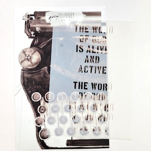 Op de afbeelding: Een witte stencil met de tekst "The word of God is alive and active. The word of God is at work if you would believe." De stencil is geplaatst op een vintage typemachine.