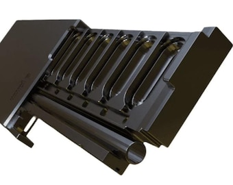 May include: A black metal tool with multiple curved slots and a cylindrical component. The tool has a rectangular shape with a slanted top and is designed for a specific purpose. The overall design is industrial and functional.