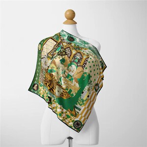 Peut inclure: Un foulard carré en soie avec un motif détaillé dans les tons de vert, or et crème. Le motif comprend des motifs animaliers et architecturaux, avec une bordure noire. Le foulard est drapé sur un mannequin.
