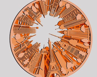 May include: An orange paper cut-out design of a city skyline with buildings and trees. The design is in a circle and the buildings are arranged around the outside of the circle, with the tops of the buildings pointing towards the center of the circle.