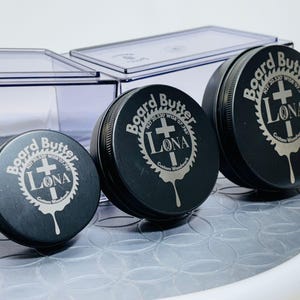 May include: Three black metal tins with the words "Board Butter" and "Lona Custom Woodwork" engraved on the lids. The lids are different sizes.