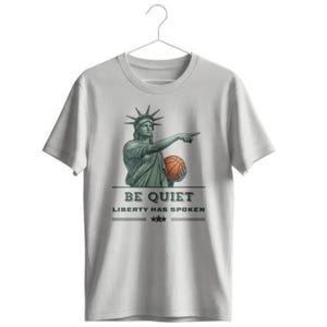 Può includere: Una t-shirt a maniche corte grigio chiaro con una grafica della Statua della Libertà che tiene in mano un pallone da basket arancione e indica. Sotto la grafica, il testo recita BE QUIET LIBERTY HAS SPOKEN con tre stelle tra due linee.