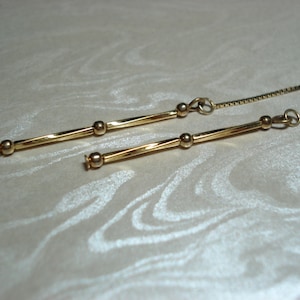 May include: A pair of gold-toned earrings with a delicate chain and a long, thin bar with small round beads.