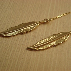 May include: A pair of gold feather earrings with a delicate chain.