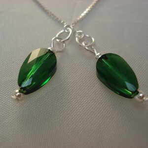 May include: A silver chain necklace with two green crystal teardrop pendants.