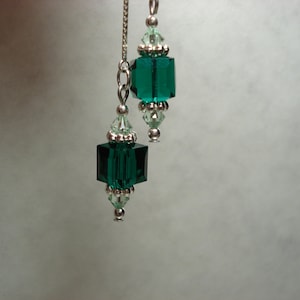 May include: Elegant dangle earrings featuring emerald green, faceted crystal beads. The earrings have a silver chain and accents, with a combination of square and round crystal shapes. The design is simple yet sophisticated, suitable for special occasions.