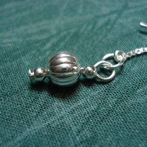 May include: Silver chain with a decorative round bead. The bead has a ribbed texture.