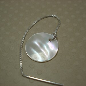 May include: A silver chain earring with a round, white mother-of-pearl pendant.