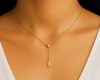 May include: A delicate gold necklace with a Y-shaped design. The necklace features a small, round, clear gemstone at the top and a larger, oval-shaped gemstone at the bottom. The chain is thin and the necklace is worn on a person.