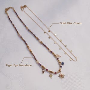 May include: A Tiger Eye necklace featuring multi-colored beads, gold-toned spacers, and charms including a star and a sun, alongside a gold disc chain necklace. The image includes the text labels Tiger Eye Necklace and Gold Disc Chain.