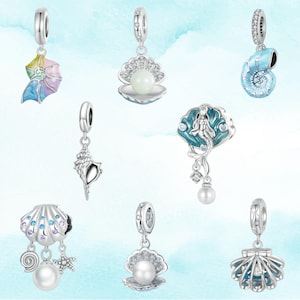 May include: A collection of silver-toned charm pendants featuring ocean-themed designs. The charms include seashells, pearls, and a mermaid, with colorful enamel accents. These pendants are designed to be added to a bracelet or necklace.