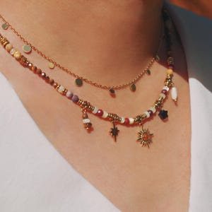 May include: A layered necklace set featuring a gold chain with small flat circular discs and a second strand composed of multi-colored beads, gold-toned spacers, and dangling charms including a starburst, a sun, and a dark star-shaped bead.