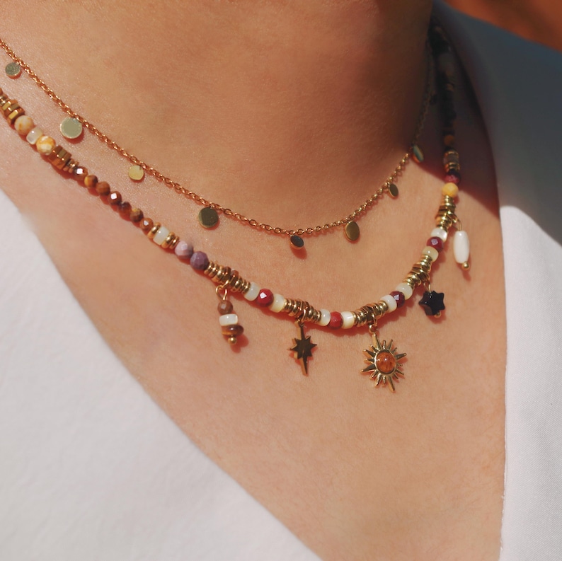 May include: A layered necklace set featuring a gold chain with small flat circular discs and a second strand composed of multi-colored beads, gold-toned spacers, and dangling charms including a starburst, a sun, and a dark star-shaped bead.