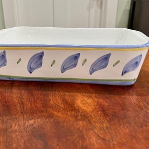 May include: Rectangular white ceramic baking dish with a blue, yellow, and green floral design. The dish features a white interior and a decorative border with blue leaf-like patterns and green accents. A classic piece for baking and serving.
