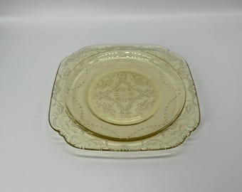 Puede incluir: Un juego de dos platos de vidrio teñido de amarillo. El plato más grande es cuadrado con un borde festoneado, y el plato más pequeño es redondo. Ambos platos presentan un diseño floral y geométrico en relieve.