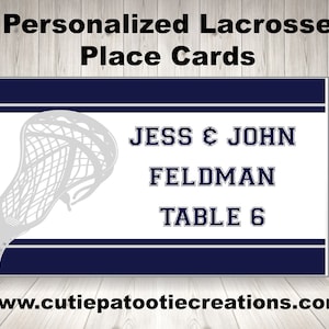 May include: White place card with a blue lacrosse stick graphic. The text reads "Jess & John Feldman Table 6".