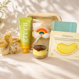 May include: A collection of beauty and self-care products, including a green tube of "green tea" face cream, a small notebook, and a packet of "Onespring" eye patches. A clear cosmetic bag and a rainbow patch are also included.