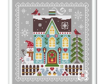 May include: A cross-stitch pattern featuring a blue and white house with a red door and a snowman in front. The house has a brown roof and white trim. There are two trees on either side of the house, one with a red cardinal on top. The pattern is surrounded by a white border with a gray background.