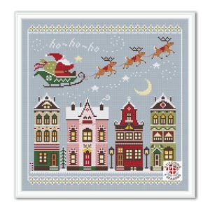 May include: A cross-stitch pattern featuring a winter scene with Santa Claus flying in his sleigh pulled by reindeer over a town with three houses. The text "ho-ho-ho" is above Santa. The pattern is on a blue background with white snowflakes.